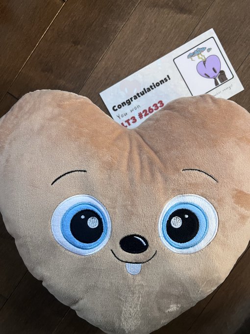 A plush pillow shaped like a cartoon poop emoji face with blue eyes and a tongue sticking out, accompanied by a card reading 'Congratulations! You won #2633' featuring a purple heart character.