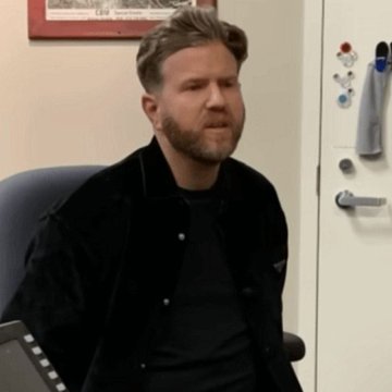 A man with a beard and a dark corduroy jacket sits in an office chair, appearing visibly distressed or emotional. The image is associated with a news report about a former U.S. police officer being sentenced to life plus 15 years for kidnapping a teen and stealing $350,000 in Bitcoin ($BTC).