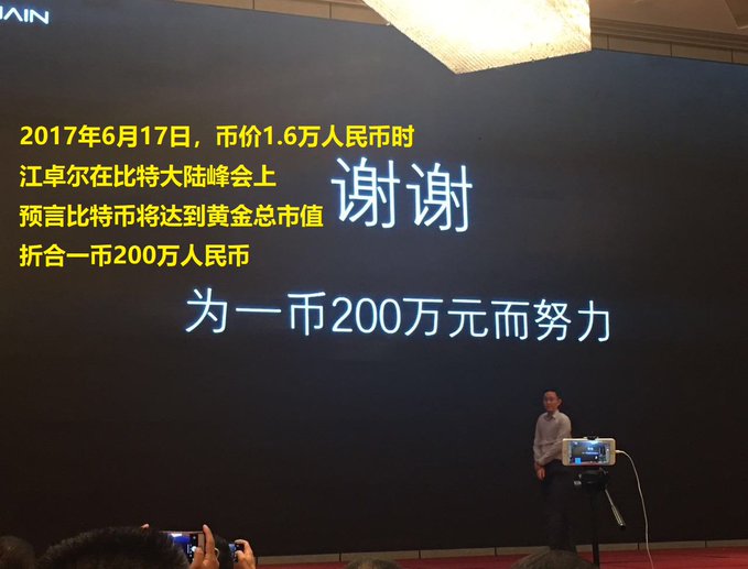 A man stands beside a large screen displaying Chinese text recalling Jiang Zhaoler's June 17, 2017 prediction at the Bitcoin Continental Summit that one coin would reach 2 million yuan, with the current price noted at 1.6万 (16,000 yuan). The prominent "谢谢" (Thank you) and "为一币200万元而努力" (Working toward one coin = 2 million yuan) emphasize the presenter's humorous, self-deprecating acknowledgment of how his optimistic prediction was made earlier than he initially remembered.