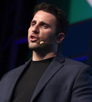 A man in a dark blazer and black shirt speaks passionately into a headset microphone, likely delivering the bold Bitcoin price prediction quoted above. His engaged expression and the professional stage setting suggest he is sharing his optimistic outlook on cryptocurrency at a public speaking event.