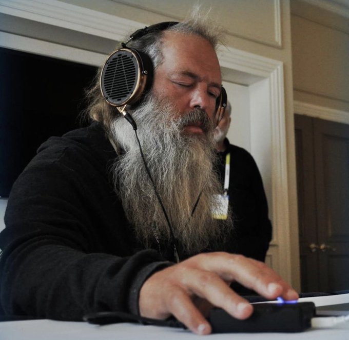 A bearded man with headphones on is intently operating a piece of audio equipment, likely engaged in a recording or listening session.