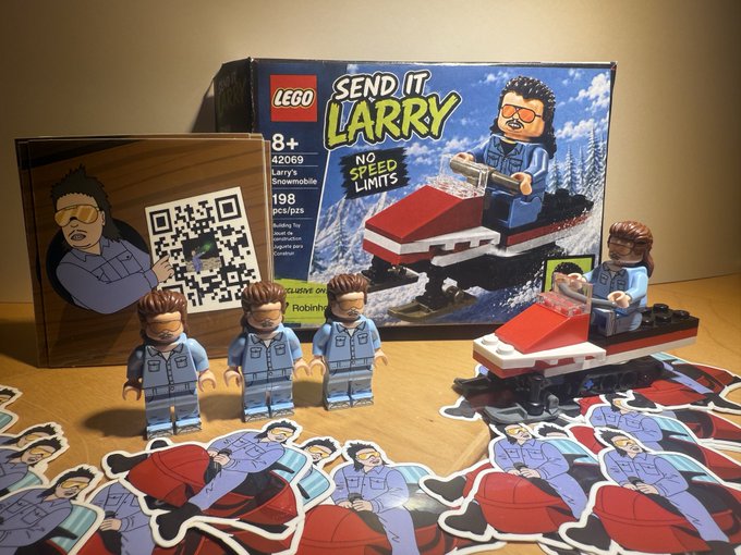 A photograph of a custom LEGO set titled 'SEND IT LARRY' featuring Larry's Snowmobile (set 42069, 198 pieces), including the box, three minifigures, a built snowmobile, and character stickers with a QR code.