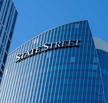 An exterior view of a modern glass skyscraper prominently displaying the 'STATE STREET' logo on its facade against a blue sky.