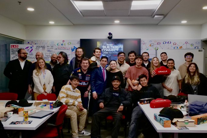 A large group photo of approximately 20 people gathered in an office space with whiteboards covered in writing, a screen displaying 'BUILDER CONNECT', and various logos including Oracle, Red Bull, and Lamborghini visible in the scene.