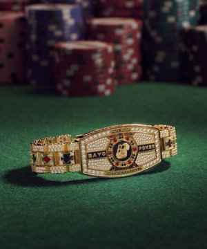 A gold and diamond-encrusted 'BAPE BAYC' bracelet rests on a green felt surface with stacks of poker chips in the background, blending streetwear and casino aesthetics.