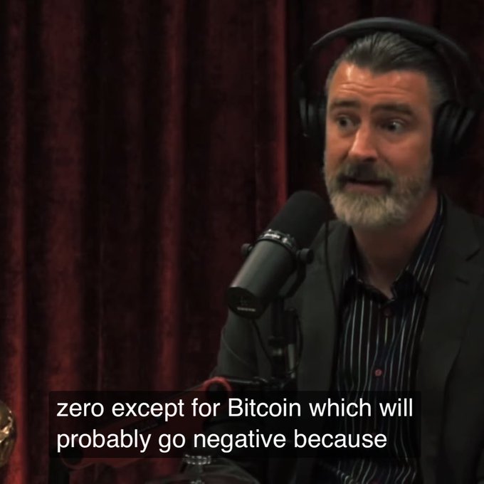A bearded man wearing headphones speaks into a microphone in a podcast setting, with subtitles reading 'zero except for Bitcoin which will probably go negative because'.