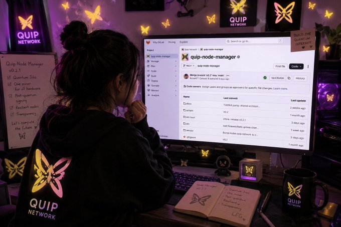 A person sits at a computer desk viewing a GitHub repository page for 'quip-node-manager', surrounded by 'QUIP NETWORK' branded items including illuminated butterfly signs, a mug, a hoodie, and a handwritten whiteboard checklist for 'Quip Node Manager v0.2.1'.