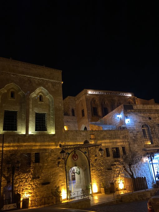 A stone building illuminated at night features a sign reading "BUREAU 47" and "THE ARCTERMINAL," with a Turkish flag displayed near the entrance. The post appears to be a thinly veiled advertisement for "The Arc Terminal," using the historic-looking architecture as a backdrop to lend an air of legitimacy and prestige to the product.