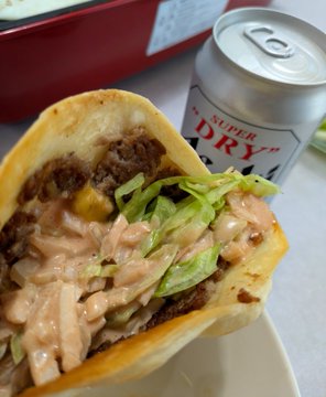 A close-up of a pita sandwich filled with meat, lettuce, and sauce, sitting next to a can of Asahi Super Dry beer.
