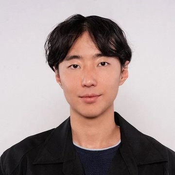 A headshot portrait of a young man with dark hair wearing a black jacket over a dark blue shirt against a white background.