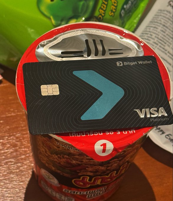 A Bitget Wallet Visa Platinum debit card rests on an opened instant noodle cup, humorously illustrating one of its everyday uses as a convenient tool even for quick meals.