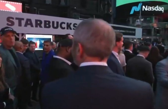 A busy scene outside the Starbucks store at the Nasdaq MarketSite in Times Square, with crowds of people and prominent signage displaying "STARBUCKS" and the "Nasdaq" logo. The image appears to capture buzz around a rumored acquisition or partnership, fitting the post's playful suggestion of Ripple potentially rebranding in connection with Starbucks.
