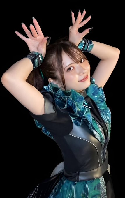 A young woman posing with her hands raised above her head, wearing an ornate blue and black dress with ruffled details.