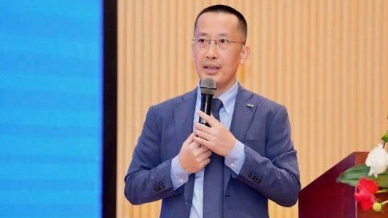 A man in a blue suit and tie speaks into a microphone at a podium, identified by context as Mr. Vũ Thành Trung, Vice Chairman of MB, discussing banks entering the digital assets space.