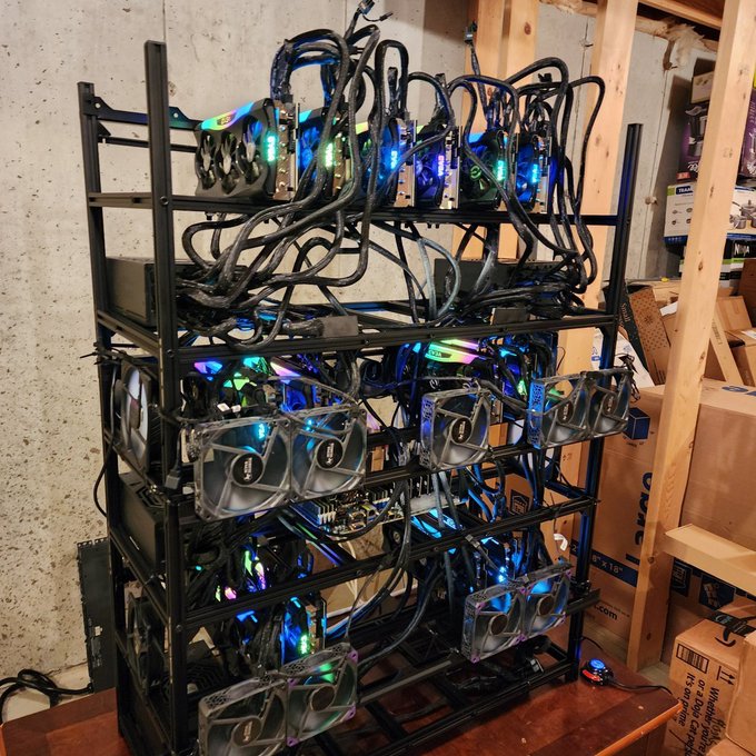 The image shows a custom-built, multi-tiered GPU mining-style PC rig with multiple graphics cards (some labeled "XFX" and "Radeon") arranged on open metal frames, illuminated by colorful RGB lighting. The setup, filled with tangled cables and exposed cooling fans, appears to be the powerful local hardware referenced in the post for running the AI model "Kimi K3" directly on the user's PC.
