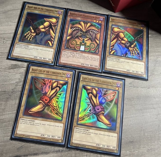 Five Yu-Gi-Oh! trading cards laid out on a wooden surface, featuring 'Exodia the Forbidden One' and its limbs (Right Arm, Left Arm, Right Leg, Left Leg), all Spellcaster-type monsters.