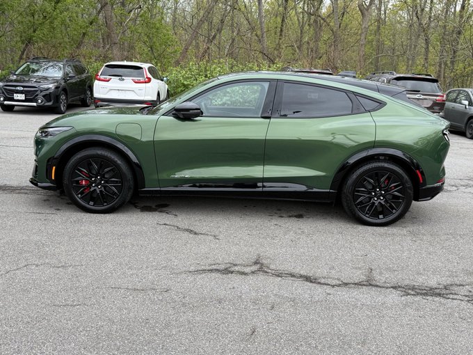 iced green car with black rims and silver wheels, parked on a gray asphalt surface surrounded by trees and other cars.