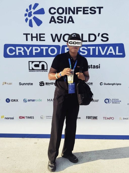 Man in black clothing standing in front of a COINFEST ASIA backdrop reading 'THE WORLD'S CRYPTO FESTIVAL' with various sponsor logos including IDX, IDRX, and Amanode.
