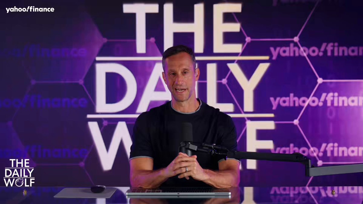 The image features a man sitting at a desk with a microphone, holding a microphone stand, and wearing a black shirt. The background of the image has purple and white hexagons arranged in a grid pattern. The caption below the image reads "Scott dropping the Bitcoin origin story with this clean, high-signal video is exactly the kind of educational content the space needs right now".