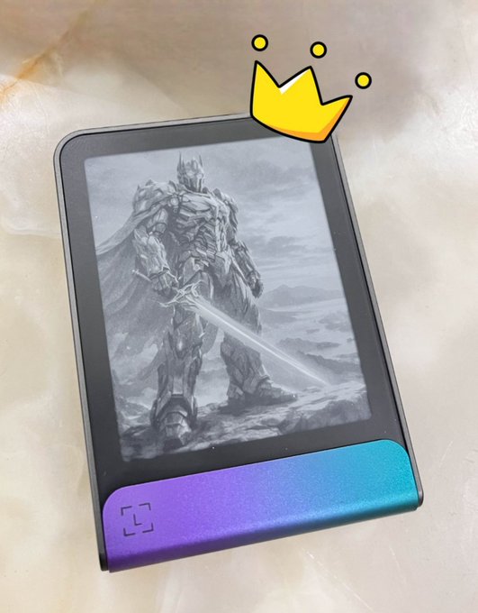 A small e-reader device with an iridescent purple-blue casing displays a grayscale fantasy illustration of an armored knight wielding a sword, with a yellow cartoon crown doodle drawn above the screen.