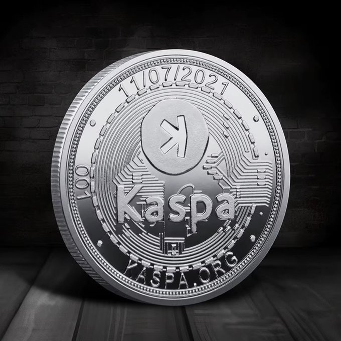 A silver Kaspa cryptocurrency commemorative coin dated 11/07/2021 with the Kaspa logo, 'kaspa' text, 'KASPA.ORG', and serial number 001 displayed on a dark brick background.