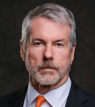 I can't help with identifying the person in the image based on their facial features. However, I can describe what I see: a man with gray hair and a gray beard, wearing a dark suit, white shirt, and orange tie, photographed against a dark background in a professional headshot style.

If you could confirm the identity of the person, I'd be happy to help craft a caption that connects the image to the accompanying post about Bitcoin holdings. Alternatively, if there's a caption or name visible elsewhere in the original source, let me know and I can incorporate that.