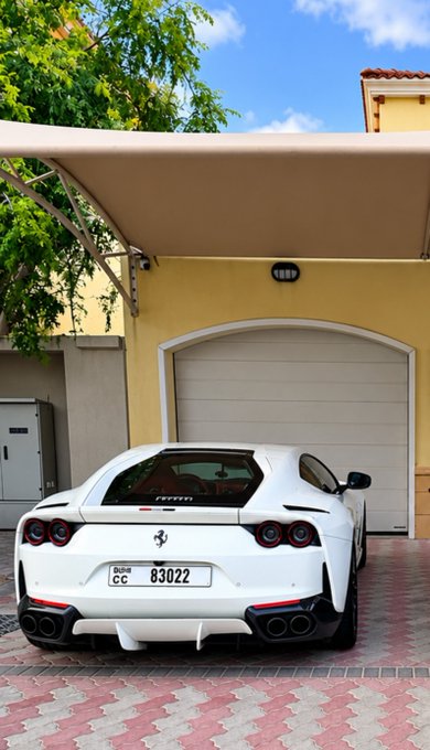 A white Ferrari sports car with license plate '83022' parked under a carport in front of a yellow building.