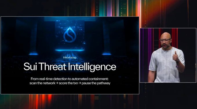 A presenter stands on stage beside a large screen announcing "Introducing Sui Threat Intelligence," with the tagline "From real-time detection to automated containment: scan the network → score the txn → pause the pathway." The presentation visually supports the announcement of this new security tool designed to detect vulnerabilities and contain threats on the Sui blockchain.