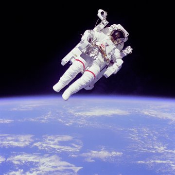 An astronaut in a white spacesuit floats untethered above Earth against the black void of space, equipped with a bulky Manned Maneuvering Unit backpack for independent movement. The image serves as a striking visual metaphor for the post's message about the contrast between seeking wealth through mundane means and pursuing extraordinary, history-making experiences in life.
