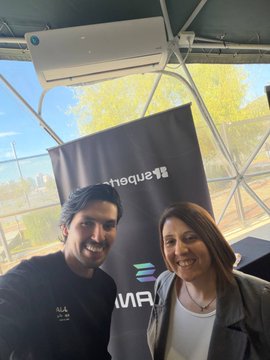 Two people smile for a photo in front of a banner that includes 'ethereum' and 'UMA' logos at what appears to be a blockchain conference.