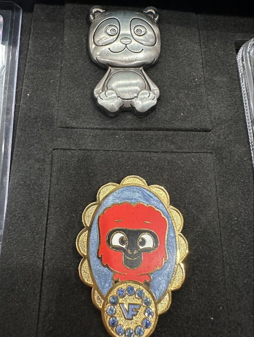 A display case holding a small silver panda figurine above a decorative pin featuring a red-haired cartoon character with a 'V' logo.