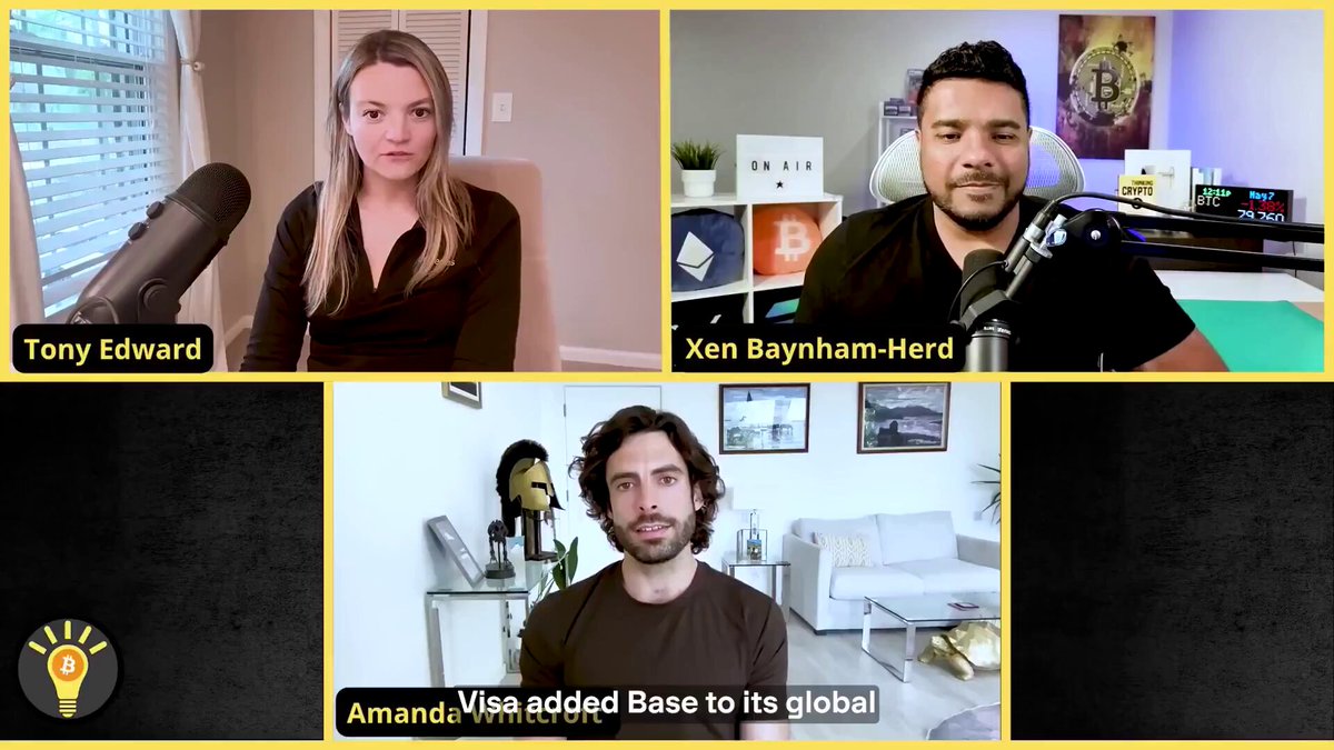 In the image, there are four people sitting around a table with microphones, appearing to be participating in an online meeting or discussion. The background shows a room with a couch and a potted plant, creating a casual atmosphere for their gathering. The main focus of the image is on the conversation happening between the individuals, as they engage in a video call using a computer screen displaying three different screens.