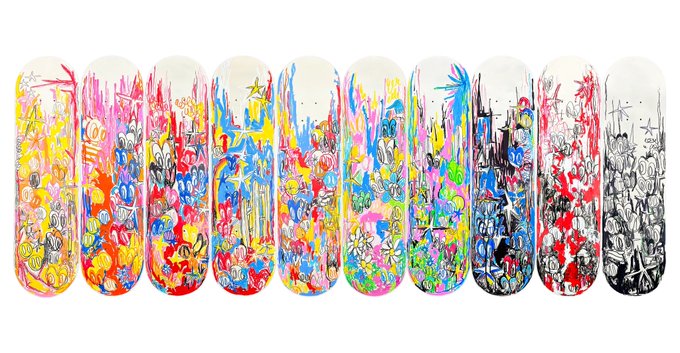 A row of ten skateboard decks displayed side-by-side, each featuring colorful, graffiti-style artwork with abstract patterns, dripping paint effects, and chaotic designs in vibrant hues, ending with one black and white deck on the far right.