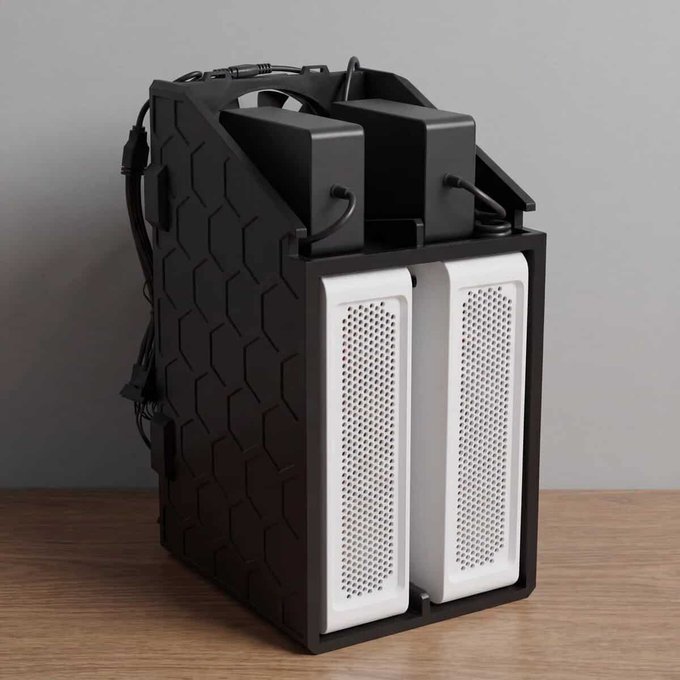 A black piece of electronic equipment, possibly a server or mining rig, with two white perforated panels on the front and cables on top, sitting on a wooden surface.