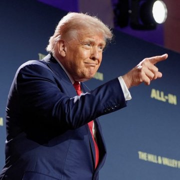 Donald Trump, dressed in a navy suit and red tie, gestures and points while speaking at a podium with "ALL-IN" and "THE HILL & VALLEY F" visible in the background, in reference to an exclusive dinner invitation for top TRUMP token holders on November 22.