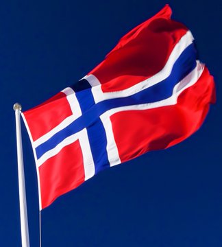The image shows the Norwegian flag waving against a clear blue sky, symbolizing Norway's sovereign wealth fund as referenced in the post. This national banner represents the fund's significant indirect exposure to approximately 11,549 Bitcoin worth $725 million through investments in companies like Strategy, Metaplanet, MARA, Coinbase, Block, and Tesla.