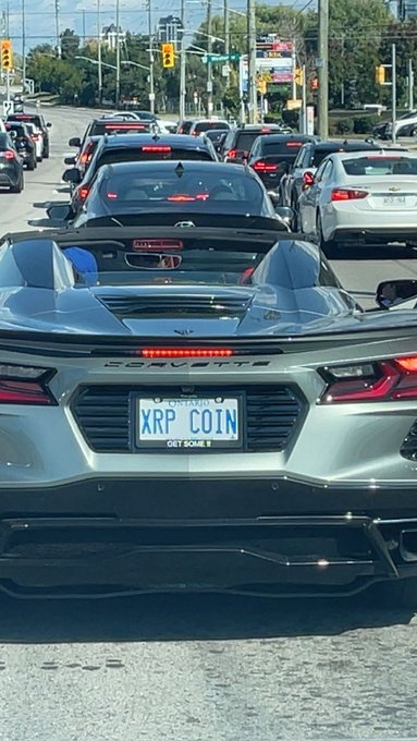 A silver Chevrolet Corvette convertible sits in Toronto traffic with an Ontario license plate reading "XRP COIN," tying into the crypto/XRP community post celebrating the personalized plate spotted in the city.