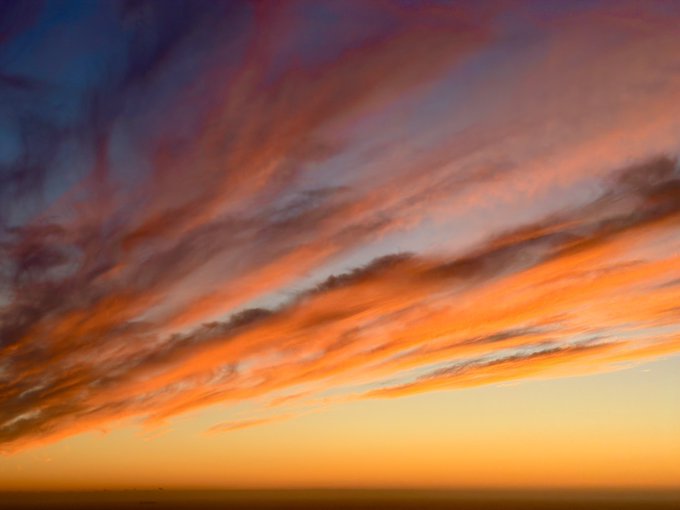 A dramatic sunset sky features streaks of orange, pink, and gray clouds stretching across the horizon at twilight.