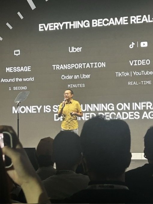 A man in a yellow shirt giving a presentation on a stage; the screen behind him reads 'EVERYTHING BECAME REAL' and references Uber and TikTok/YouTube.