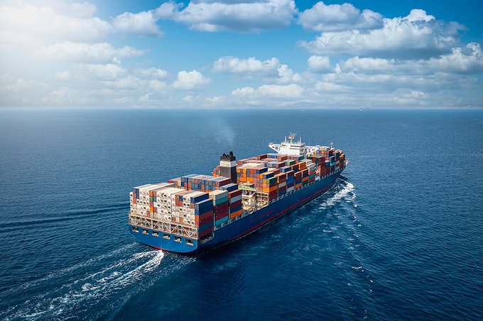 Aerial photograph of a large blue container ship loaded with colorful shipping containers sailing through the ocean.