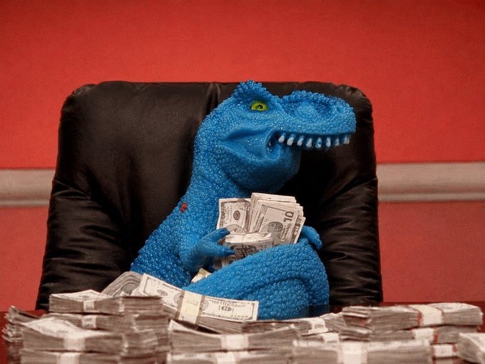 A blue toy dinosaur sits in a black leather office chair, casually holding a stack of $10 bills while surrounded by piles of cash on a desk, evoking the suspicious "got rich quick" meme energy referenced by the ticker $FEFER.