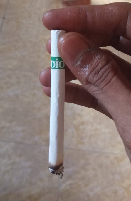 A hand holds a burnt-out cigarette with "Dio" visible on the filter, while the post expresses frustration about still waiting for success and wishing to be like others who always win. The smoking imagery symbolizes the lingering, anxious wait for a victory that never seems to arrive.
