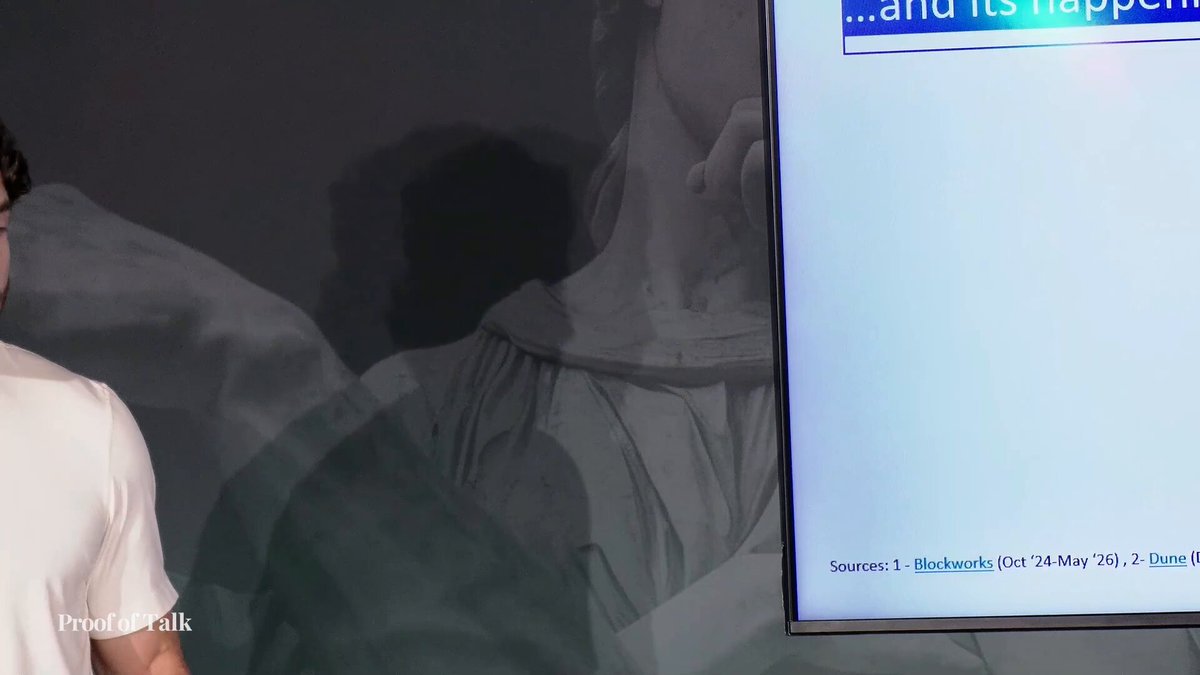 The image shows a person standing next to a computer monitor, with a banner that reads "And It's Happening" above them. The background of the image is black, which contrasts with the white text on the banner. The person appears to be in front of a television screen or a projection screen, and there are some words written below the banner.