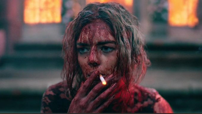 urn of blood on a woman's face, with red lipstick and a cigarette in her mouth, set against a blurred background.