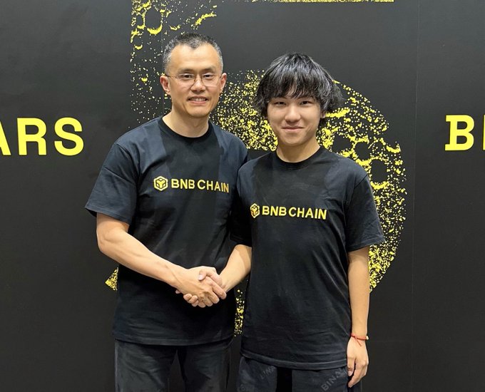 Two men wearing black "BNB CHAIN" t-shirts shaking hands in front of a black and yellow backdrop.