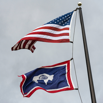 The American flag and the Wyoming state flag fly from a flagpole against a gray sky.