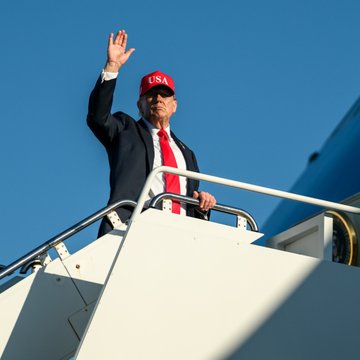 Donald Trump waves from the stairs of a plane while wearing a red "USA" cap and tie, an image often used to illustrate his public appearances as news circulates about his 2025 financial disclosure revealing over $100 million in combined Bitcoin and Ethereum holdings.