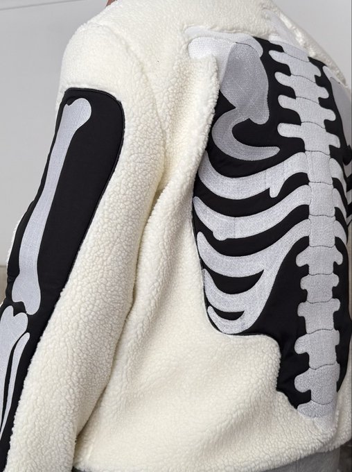 A close-up of a cream-colored fleece jacket featuring a black and white skeleton ribcage and arm bones design.