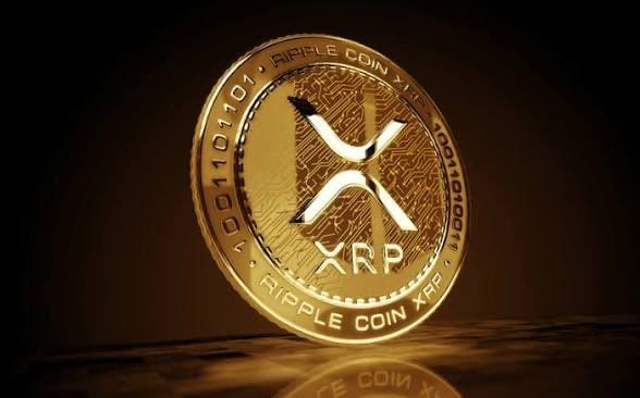 A close-up of a gold Ripple Coin (XRP) with binary code and circuit patterns engraved around its edge, resting on a dark reflective surface.