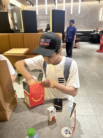 A young boy wearing a "Feel the Future" cap is opening a McDonald's Happy Meal box, with a smaller meal box and a small bottle on the table. The post "This is who you're trading against" suggests the image humorously implies that even young kids might be engaged in trading or market activities, highlighting the accessibility and pervasiveness of trading in modern society.